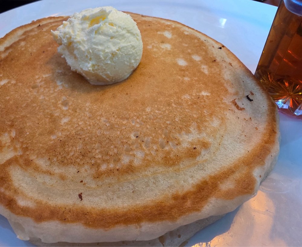 A tall stack of golden buttermilk pancakes drizzled with maple syrup